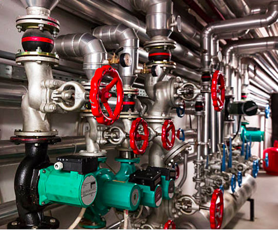 Image of a maze of metal gas or water pipes with bright red control wheels